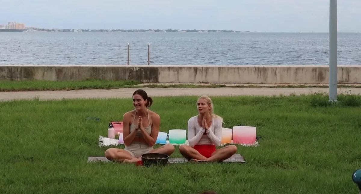 Two women seated in an outdoor yoga class by the water