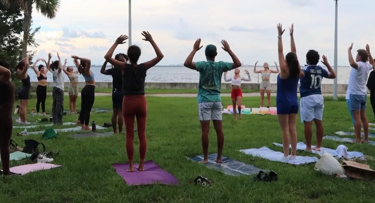 An outdoor yoga class standing together with arms raised